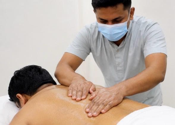 Therapist working warm herbal oil into a patient's back with steady, even pressure.